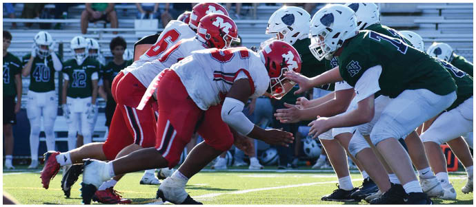 Two opposing American football teams are lined up at the line of scrimmage with players in red and white uniforms crouched ready to start the play against players in green and white uniforms. Description generated by AI