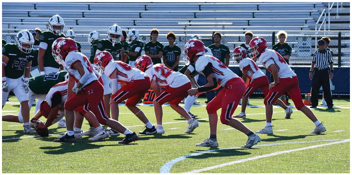 Players in red and white football uniforms are actively engaged in a tackle on a green field during a game. Description generated by AI
