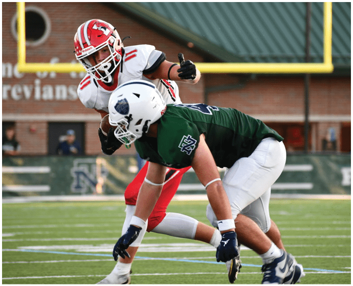 Two people in football uniforms are engaged in a play on a football field with one person in a red and white uniform giving a thumbs-up while the other in a green and white uniform is bent forward. Description generated by AI