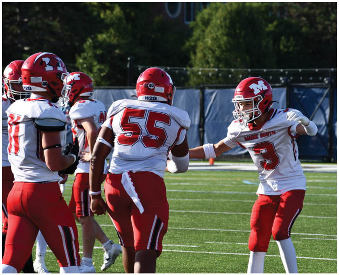 Several people wearing red and white football uniforms are on a green field, with one person in a helmet and jersey number 3 extending their arms toward another person wearing jersey number 55. Description generated by AI