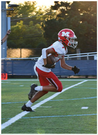 A person wearing a red helmet and red and white football uniform is running on a football field while holding a football. Description generated by AI
