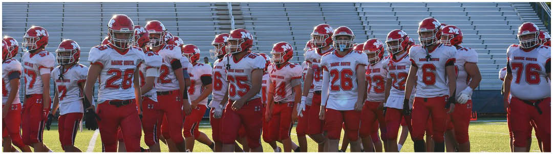 A group of people wearing white and red football uniforms and helmets are standing together on a field with empty bleachers in the background. Description generated by AI