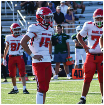 Three people in red and white football uniforms stand on a field with spectators in the background. Description generated by AI
