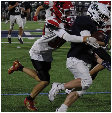 Two people in football uniforms are engaged in a tackle on a grassy field during a game. Description generated by AI