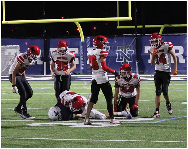 Several people in football uniforms with red helmets are gathered on a field near a goalpost, with one person lying on the ground. Description generated by AI