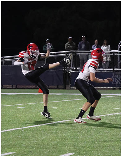 A group of people wearing football uniforms are playing on a field with one person jumping to catch a football while others are running nearby and spectators sit in the bleachers. Description generated by AI