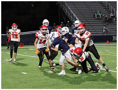 A group of people wearing football uniforms are actively playing on a field with some tackling and others running or watching. Description generated by AI