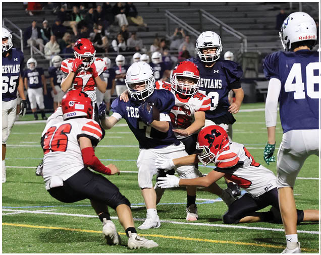 People wearing football uniforms are actively playing on a field with some players attempting to tackle or block others during a game. Description generated by AI