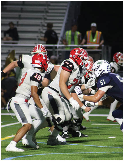 Several people wearing football uniforms and helmets are lined up on a field, preparing for a play during a game. Description generated by AI