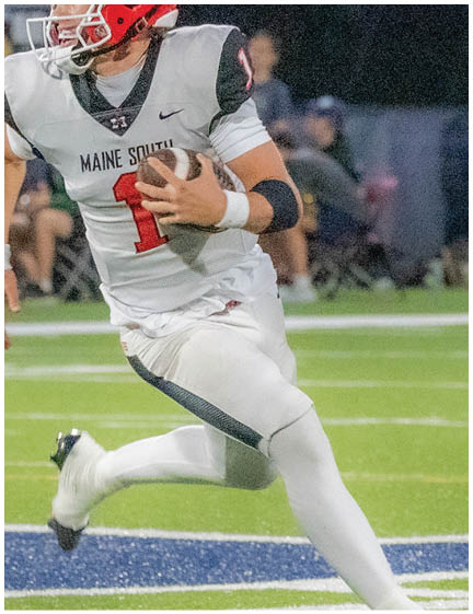 A person wearing a red helmet and white football uniform is running on a green football field while holding a football. Description generated by AI
