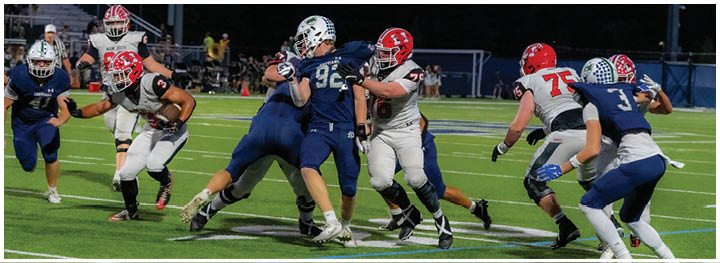 People in football uniforms are actively engaged in a play on a well-lit field during a game. Description generated by AI
