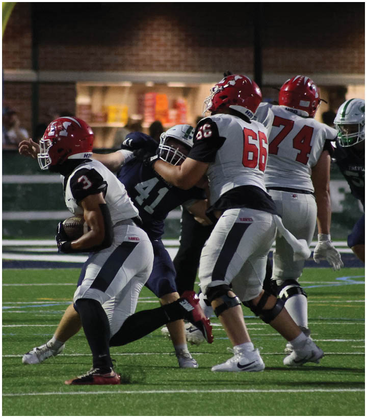 A group of people wearing football uniforms are engaged in a play on a football field near the goalpost. Description generated by AI