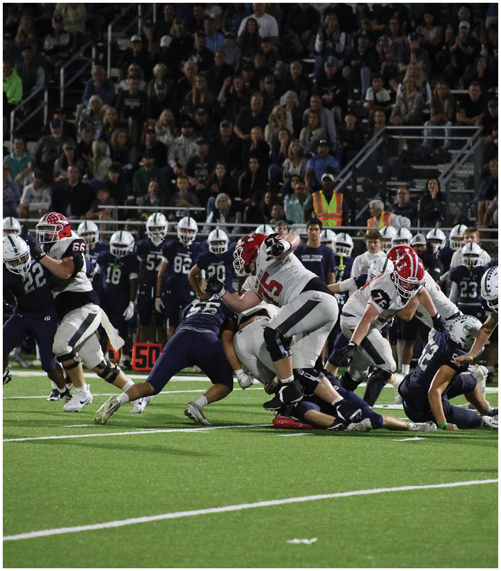 A group of people in football uniforms are actively engaged in a game on a field with a crowd watching from the stands. Description generated by AI