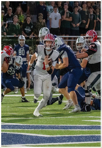 A group of people in football uniforms are actively playing on a field with a crowd watching in the background. Description generated by AI