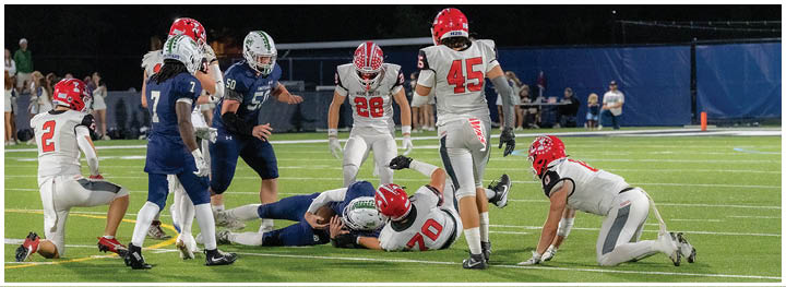 People in football uniforms are engaged in a play on a well-lit field during a nighttime game. Description generated by AI