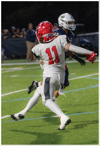 A person wearing a white football uniform with the number 11 is running on a green field during a game. Description generated by AI