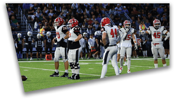 Several people in football uniforms stand on a field with a football on the ground and a crowd in the background. Description generated by AI