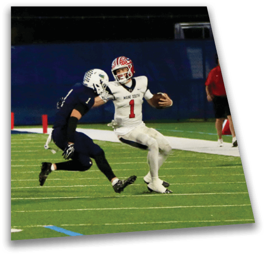 Two people in football uniforms are actively engaged in a play on a green field with yard lines and a dark blue background. Description generated by AI