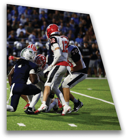 Four people in football uniforms are engaged in a play on a green field with a blurred crowd in the background. Description generated by AI