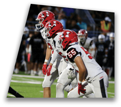 People in football uniforms are positioned on a field preparing for a play during a game. Description generated by AI