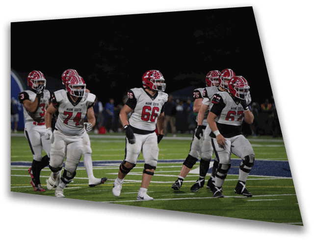Several people wearing football uniforms with red helmets and white jerseys are on a football field at night. Description generated by AI