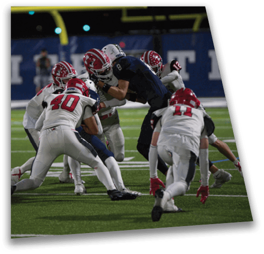 Several people in football uniforms are engaged in a play on a field under stadium lights near a goalpost. Description generated by AI