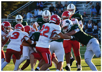 Several people wearing football uniforms are engaged in a close physical play on a football field during a game. Description generated by AI