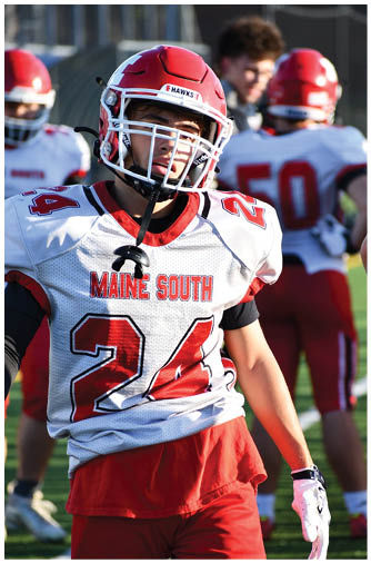 A person wearing a red football helmet and white jersey with red and black accents is on a sports field. Description generated by AI