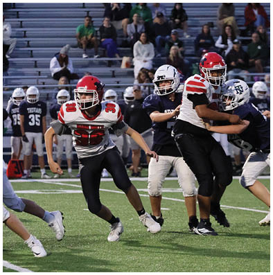 A person wearing a red helmet and white and red football uniform is running on a football field while other players and spectators are visible in the background. Description generated by AI