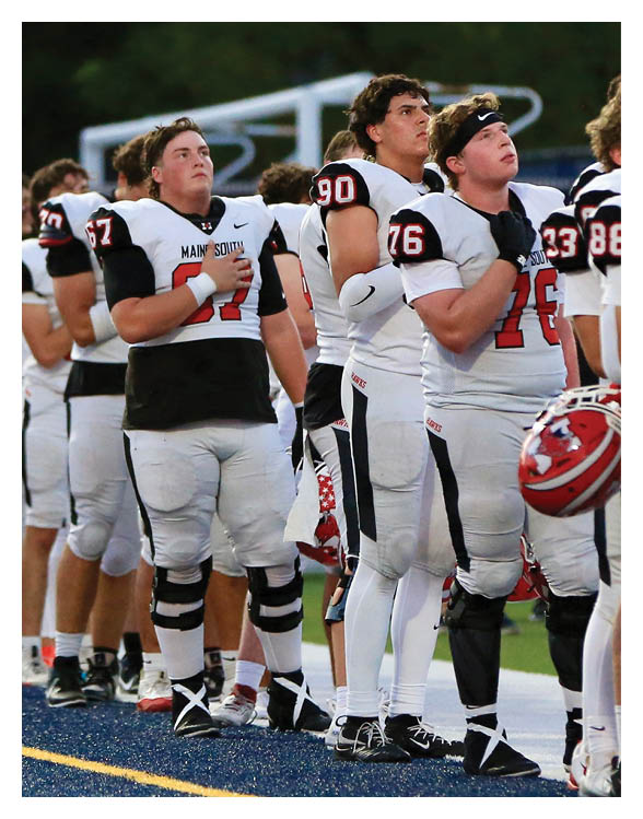 A group of people wearing football uniforms stand in a line on a field with one person holding a helmet. Description generated by AI
