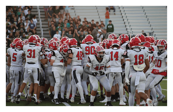 A group of people wearing white sports uniforms with black and red accents are gathered closely together on a green field. Description generated by AI
