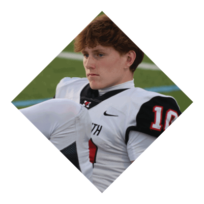 A person with short curly hair wearing a white sports jersey with black and red accents is sitting on a grassy field looking to the side. Description generated by AI