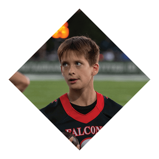 A child wearing a black and red sports jersey with the word Falcons stands on a grassy field looking slightly to the side. Description generated by AI