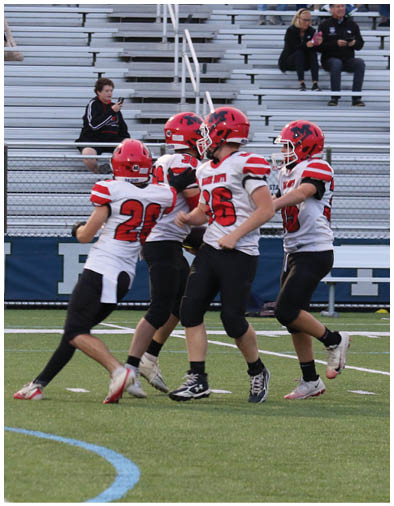 A person wearing a red and white football uniform is running on a green field with empty bleachers in the background. Description generated by AI