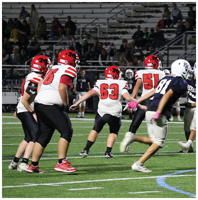 People wearing football uniforms are actively playing on a field under stadium lights with empty bleachers in the background. Description generated by AI