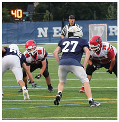 People in football uniforms are positioned on a field, appearing ready for a play during a game. Description generated by AI