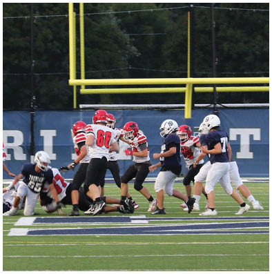 People in football uniforms are actively playing on a field with a referee observing the action. Description generated by AI