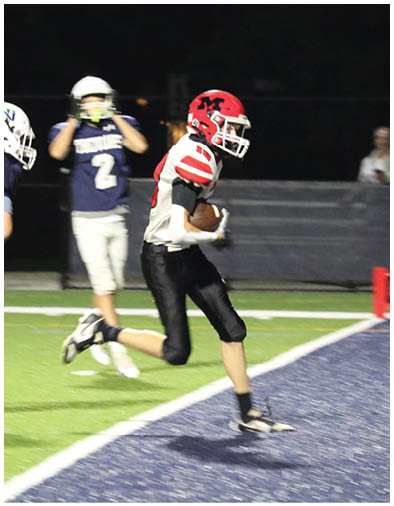 A person wearing a red helmet and white football jersey is running on a field while holding a football. Description generated by AI