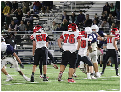 Adults wearing football uniforms in red and white and blue and white appear to be engaged in a game on a field with spectators in the background. Description generated by AI