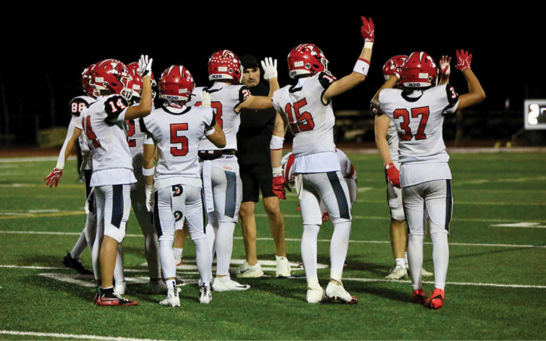 A group of people wearing white and red football uniforms are standing on a field with their hands raised, appearing to celebrate or signal. Description generated by AI