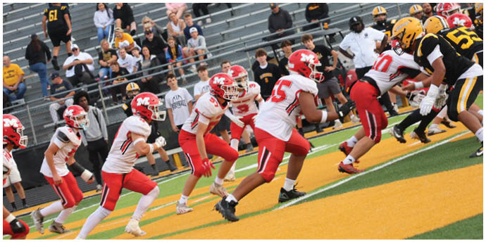 A group of people in red and white football uniforms are lined up on a field preparing for a play while spectators watch from the bleachers. Description generated by AI