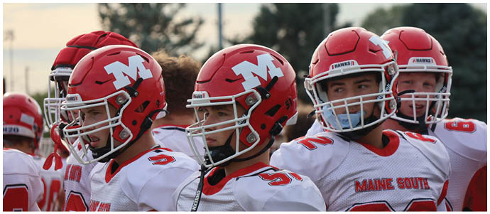 A group of people wearing red football helmets with a white “M" and white jerseys with "Maine South" written on them are standing closely together outdoors. Description generated by AI