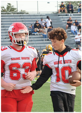 Three people wearing football uniforms with “Maine South" on their jerseys are on a field, with one person holding a football and appearing to talk to the others. Description generated by AI