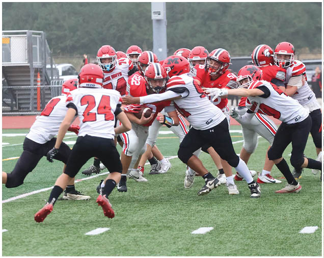 A group of people wearing red and white football uniforms are actively engaged in a play on a grassy field with one person holding the ball while others attempt to block or tackle. Description generated by AI