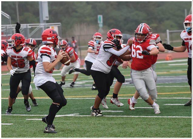 A group of people wearing football uniforms are actively engaged in a game on a field with one person preparing to throw the ball while others block and defend. Description generated by AI
