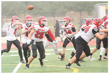 A group of people wearing red helmets and white jerseys are playing football on a field with one person throwing the ball. Description generated by AI