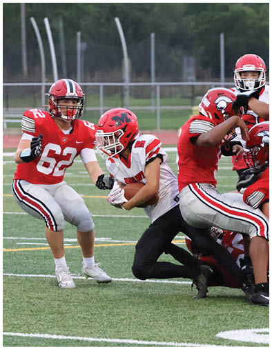Two people in football uniforms and helmets are engaged in a play on a field with one person holding the ball and the other preparing to block or tackle. Description generated by AI