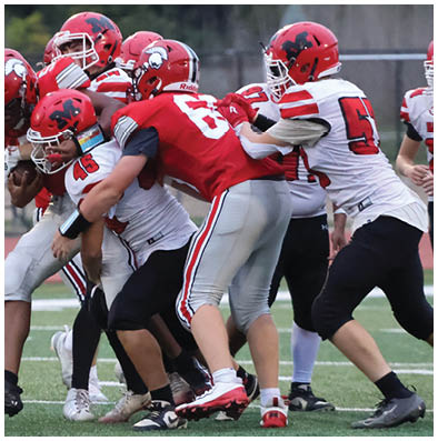 People wearing red and white football uniforms are engaged in a tackle on a green field during a game. Description generated by AI