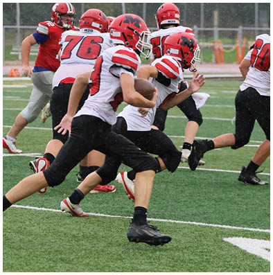 Several people wearing red and white football uniforms are actively running on a green field during a game. Description generated by AI