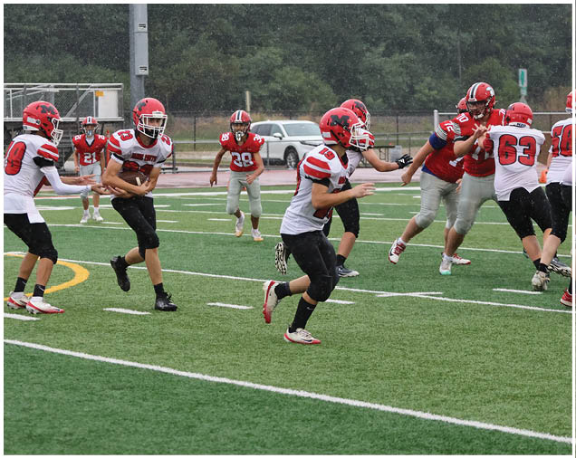 Several people in football uniforms with red helmets are gathered on a field near a goalpost, with one person lying on the ground. Description generated by AI